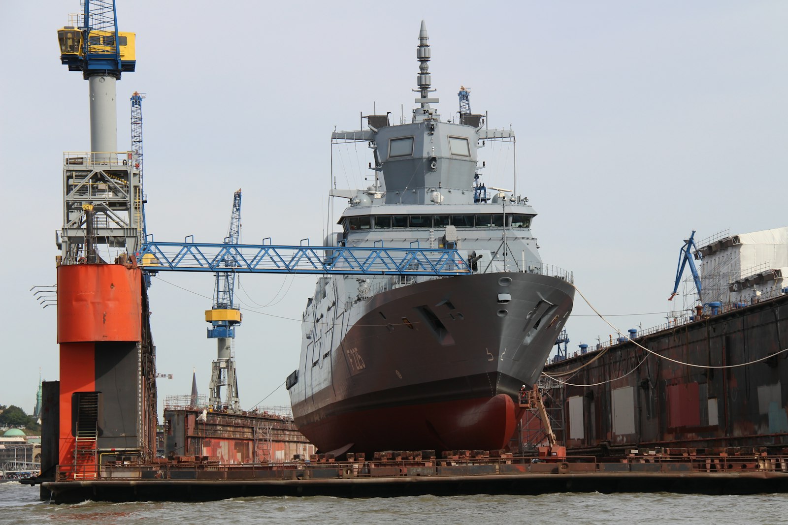 Newbuilding on a shipyard dock beneath heavy cranes